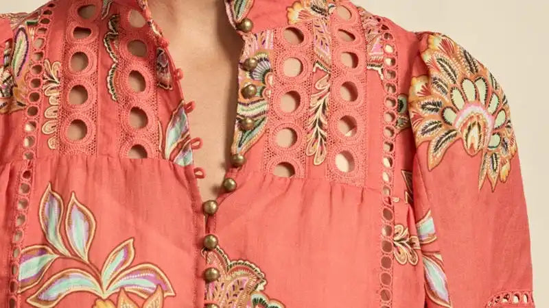 Coral-colored women’s top with floral print, eyelet details, and a button-up mandarin collar.