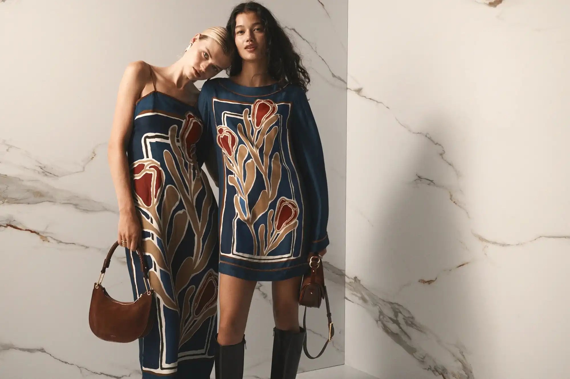 Two women posing in matching navy blue outfits with a red and gold floral pattern.