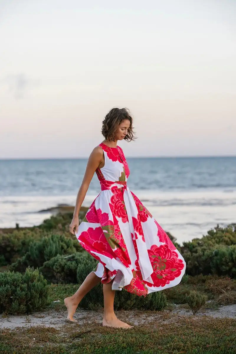 A flowing white dress with bold red and gold floral patterns, featuring a fitted bodice and flared skirt.