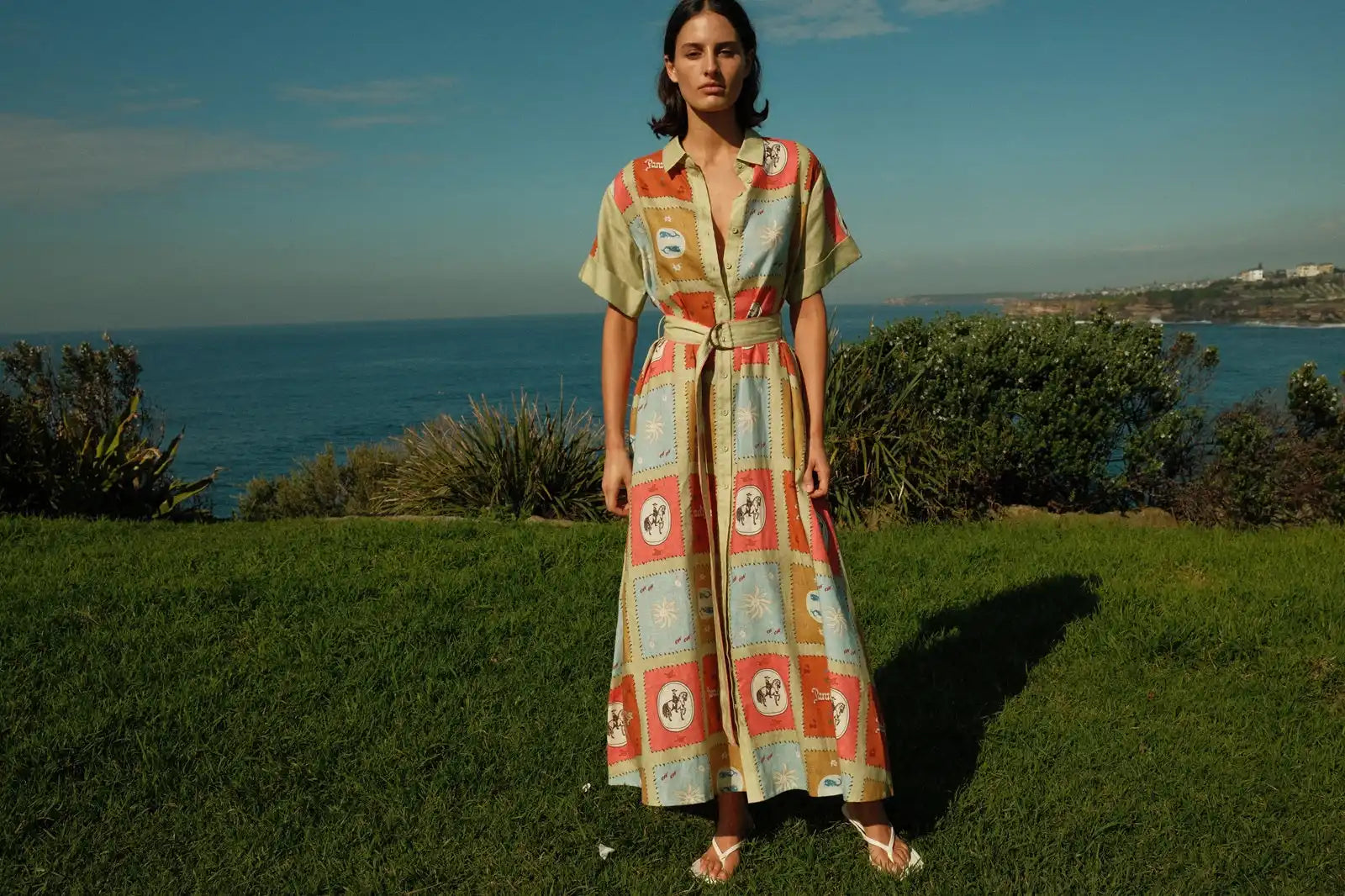 A woman wearing a patterned maxi dress with a belted waist and short sleeves.